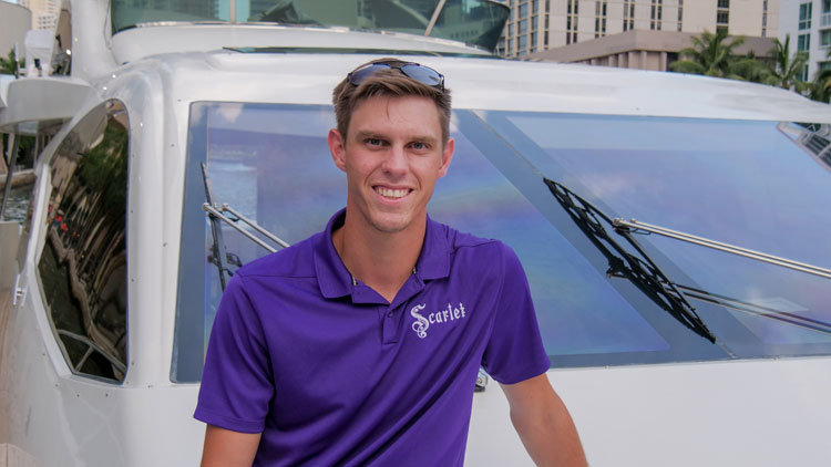 A man in a purple shirt standing in front of a white car